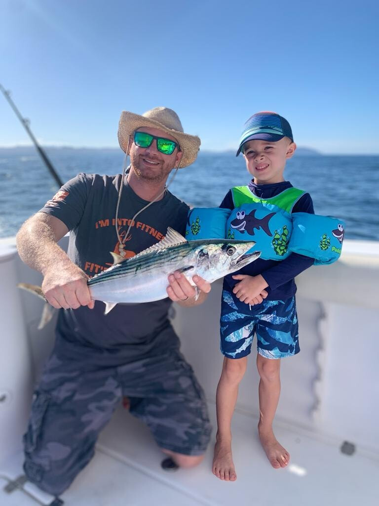 Father and son holding fish on boat